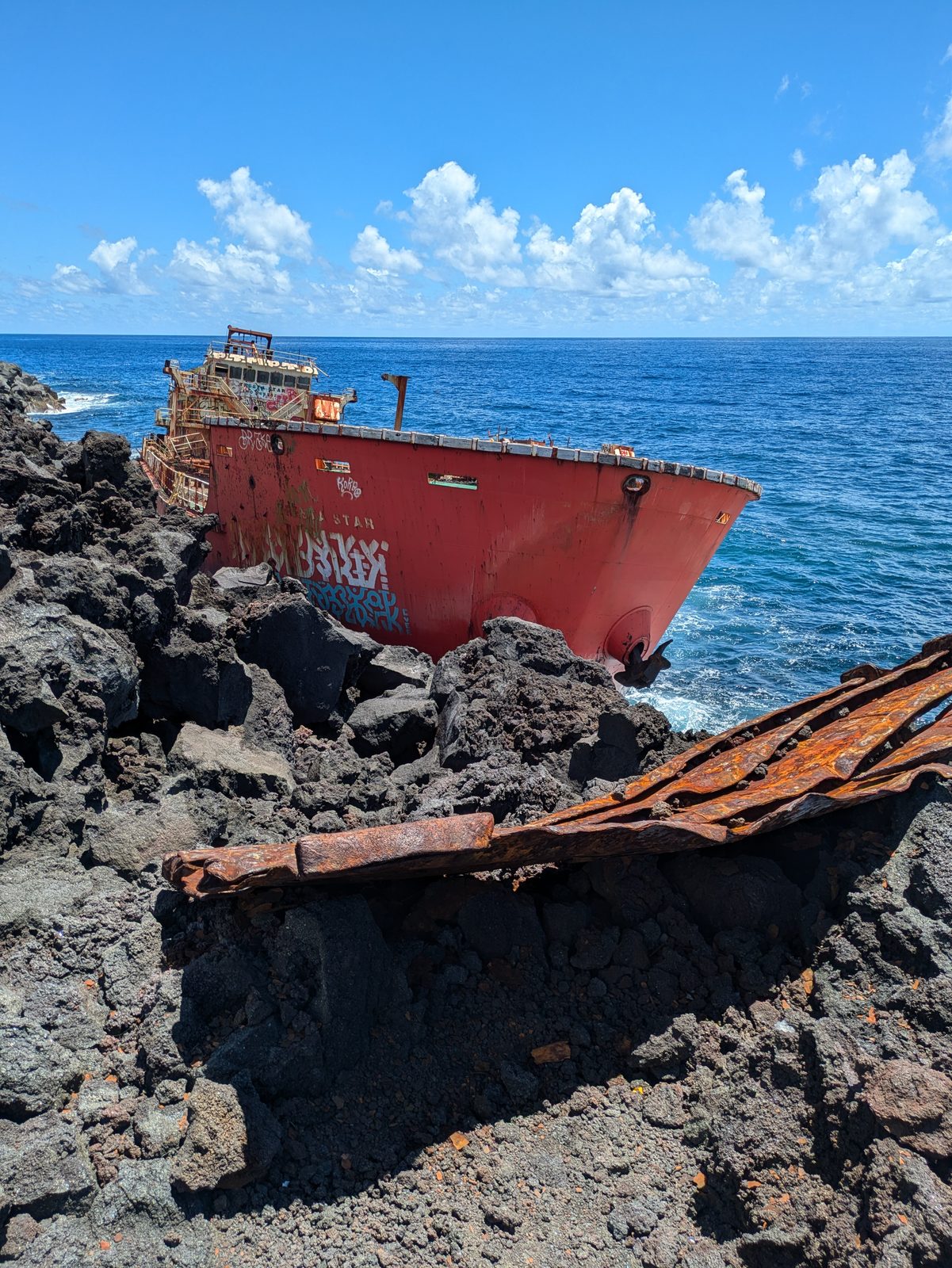 La coque rouge du cargo Tresta Star échoué sur les blocs de lave noire du Tremblet, avec des tôles rouillées au premier plan